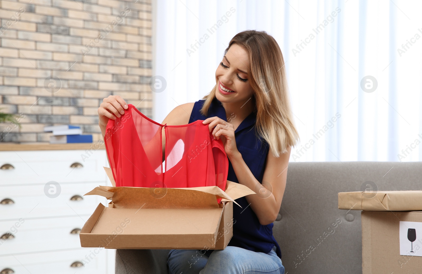 Photo of Young woman opening parcel on sofa in living room