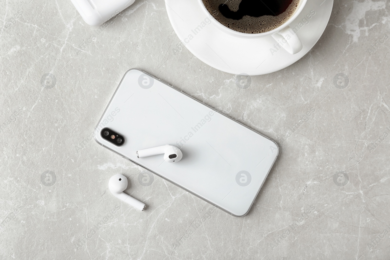 Photo of Flat lay composition with wireless earphones and mobile phone on light grey marble table