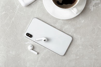 Photo of Flat lay composition with wireless earphones and mobile phone on light grey marble table