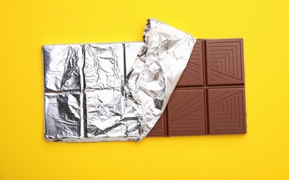 Photo of Tasty chocolate bar on yellow background, top view