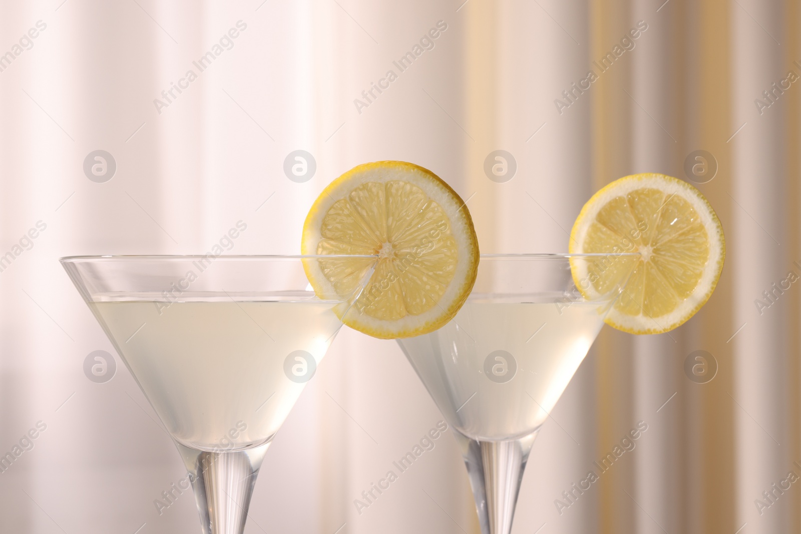 Photo of Elegant martini glasses with fresh cocktail and lemon slices near curtain, closeup