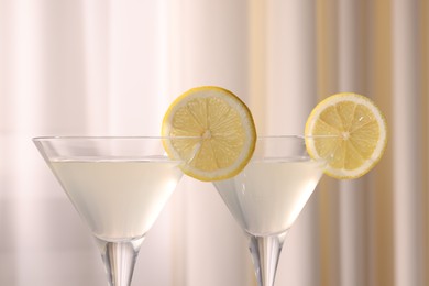 Elegant martini glasses with fresh cocktail and lemon slices near curtain, closeup