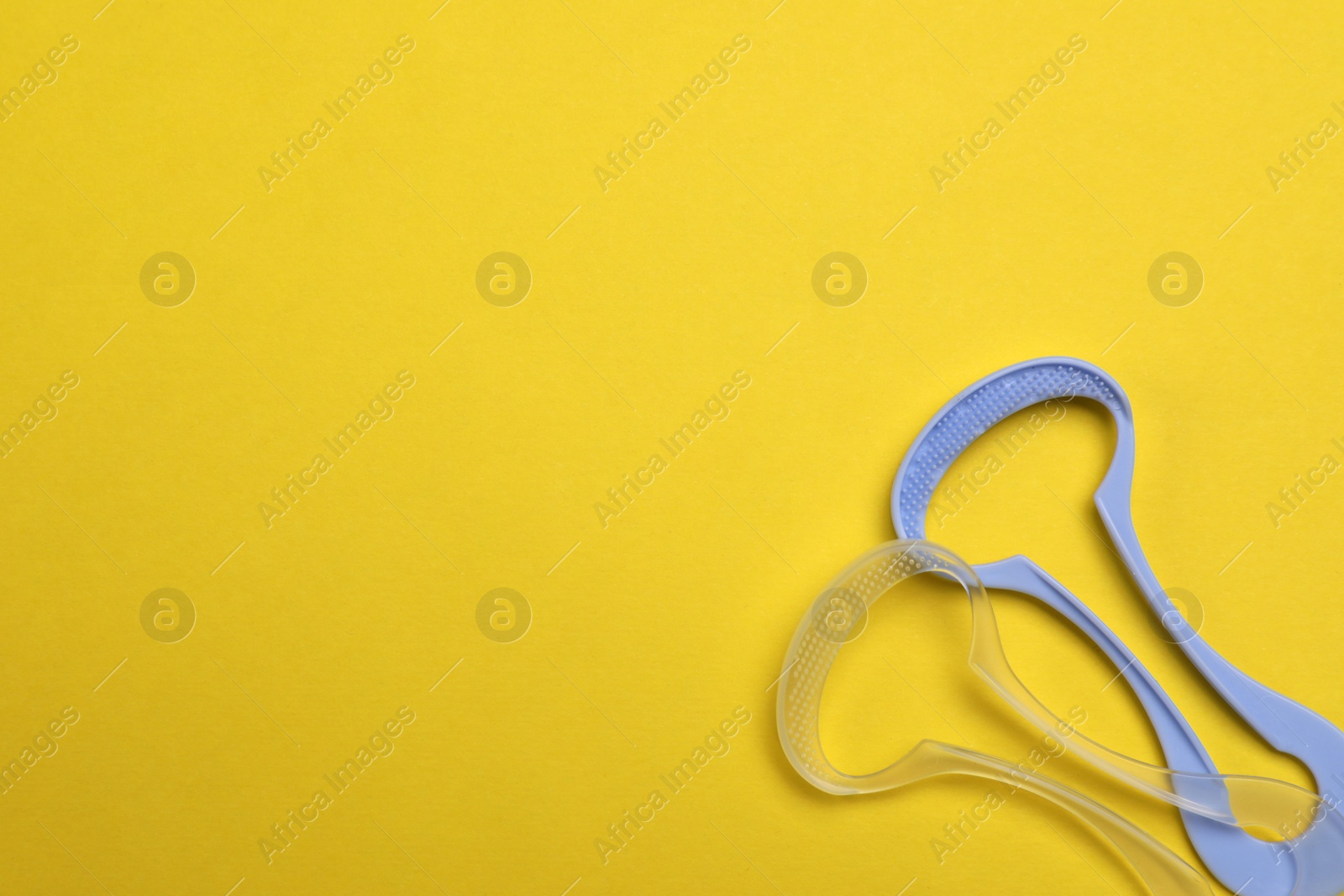 Photo of Tongue cleaners on yellow background, flat lay. Space for text