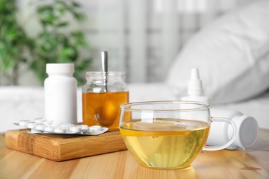 Photo of Glass cup of hot tea with lemon and different cold remedies on wooden table