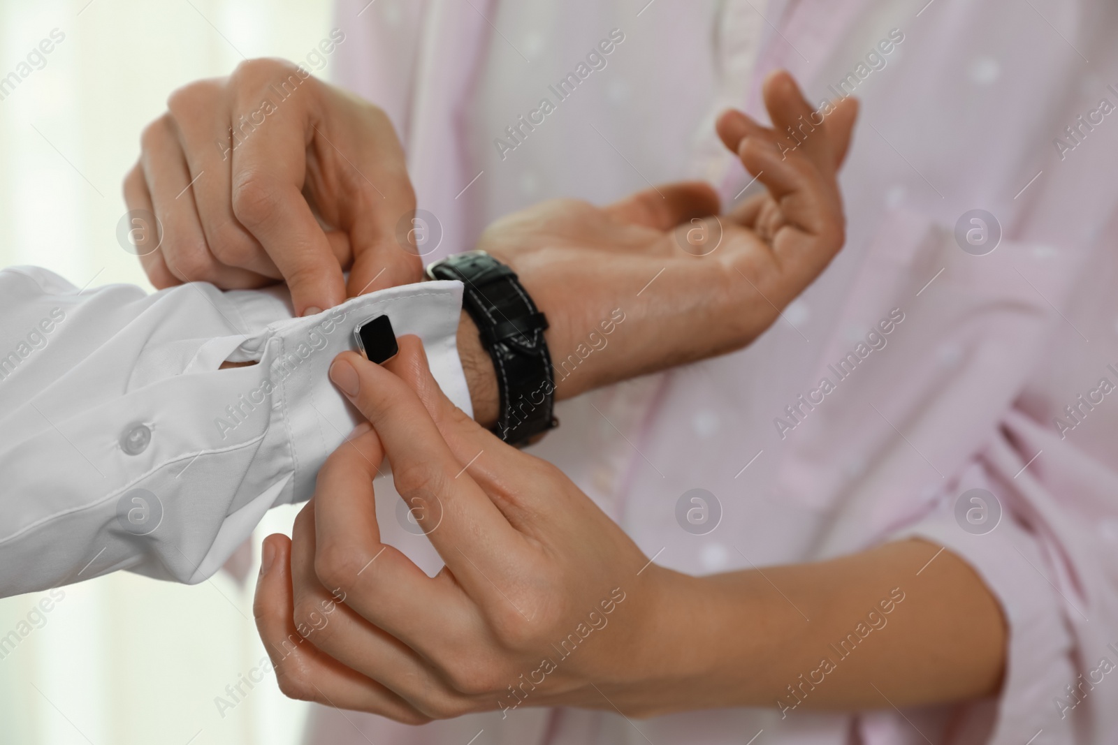 Photo of Woman helping man to put on cufflink, closeup