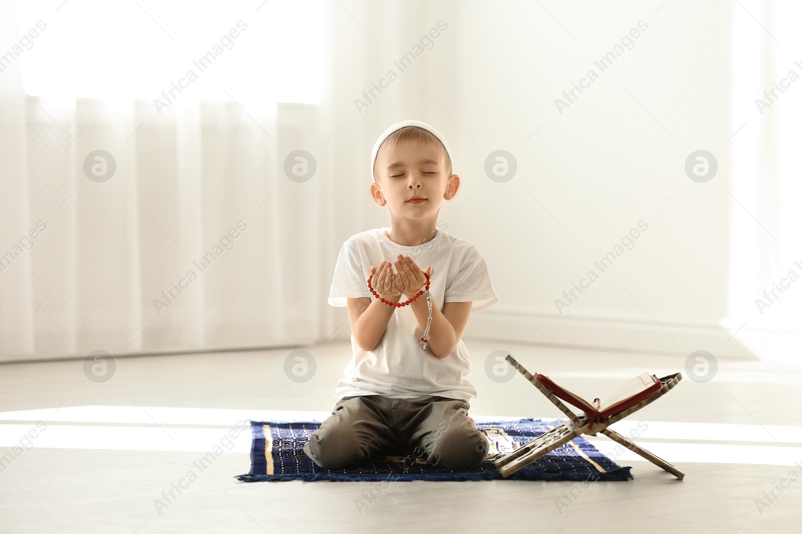 Photo of Little Muslim boy with misbaha and Koran praying on rug indoors