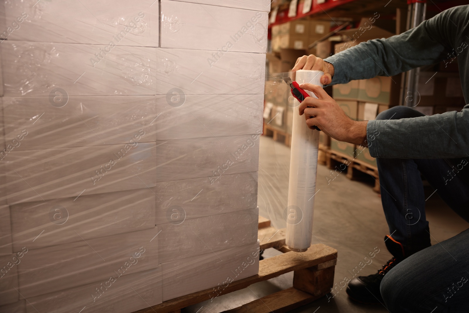 Photo of Worker wrapping boxes in stretch film at warehouse, closeup