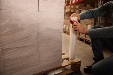 Photo of Worker wrapping boxes in stretch film at warehouse, closeup