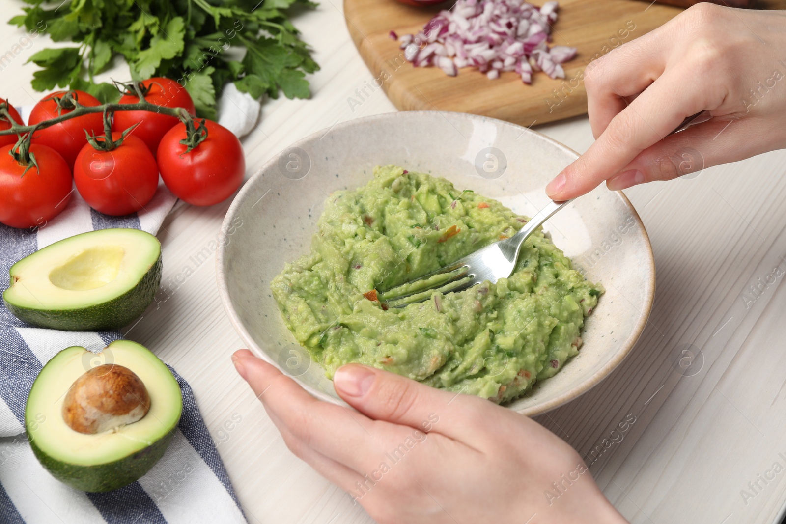 Photo of Woman preparing delicious guacamole at white wooden table, closeup