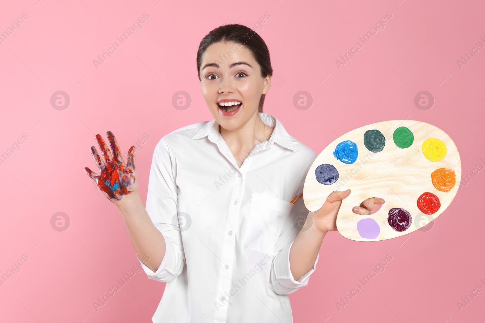Photo of Woman with painted palm and palette on pink background. Young artist
