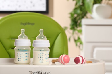 High chair with feeding bottles of infant formula and toy maracas on white tray indoors