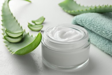 Photo of Jar with cream, cut aloe leaves and towel on white table, closeup