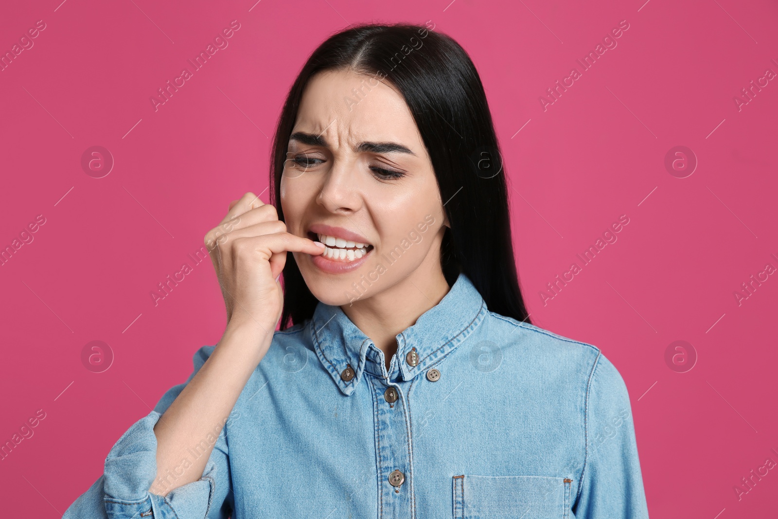 Photo of Young woman biting her nails on pink background