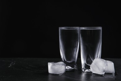Photo of Vodka in shot glasses with ice on table against black background. Space for text
