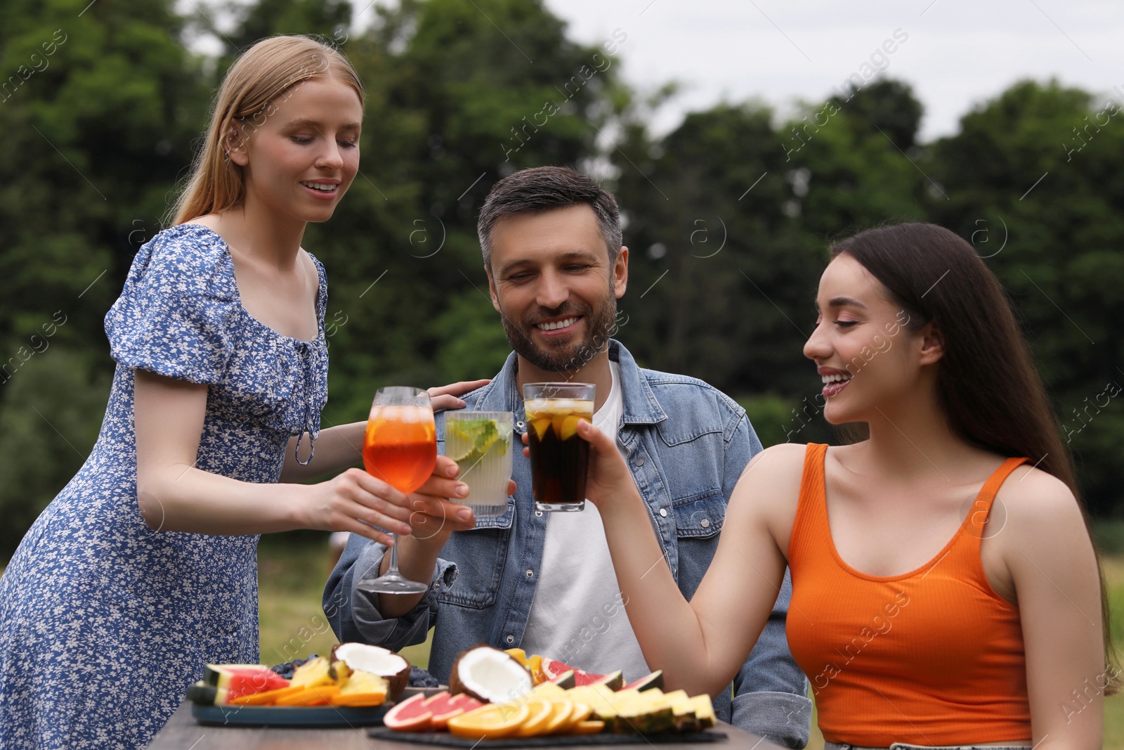 Photo of Happy friends clinking glasses with cocktails at table outdoors