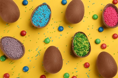 Photo of Sweet chocolate eggs with sprinkles and candies on yellow background, flat lay