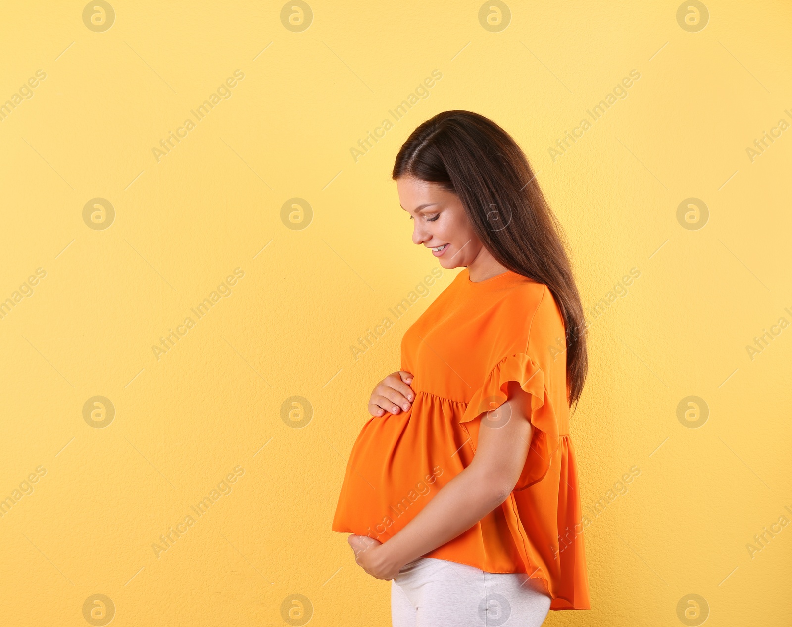 Photo of Happy pregnant woman posing on color background. Space for text