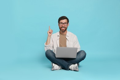 Photo of Happy handsome man with laptop sitting on light blue background