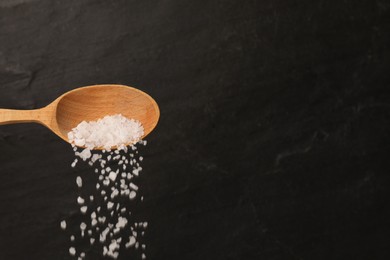 Photo of Pouring sea salt from wooden spoon against black background. Space for text