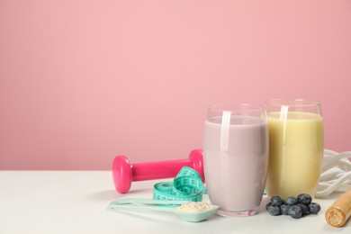 Photo of Tasty shakes with blueberries, sports equipment, measuring tape and powder on white table against pink background, space for text. Weight loss