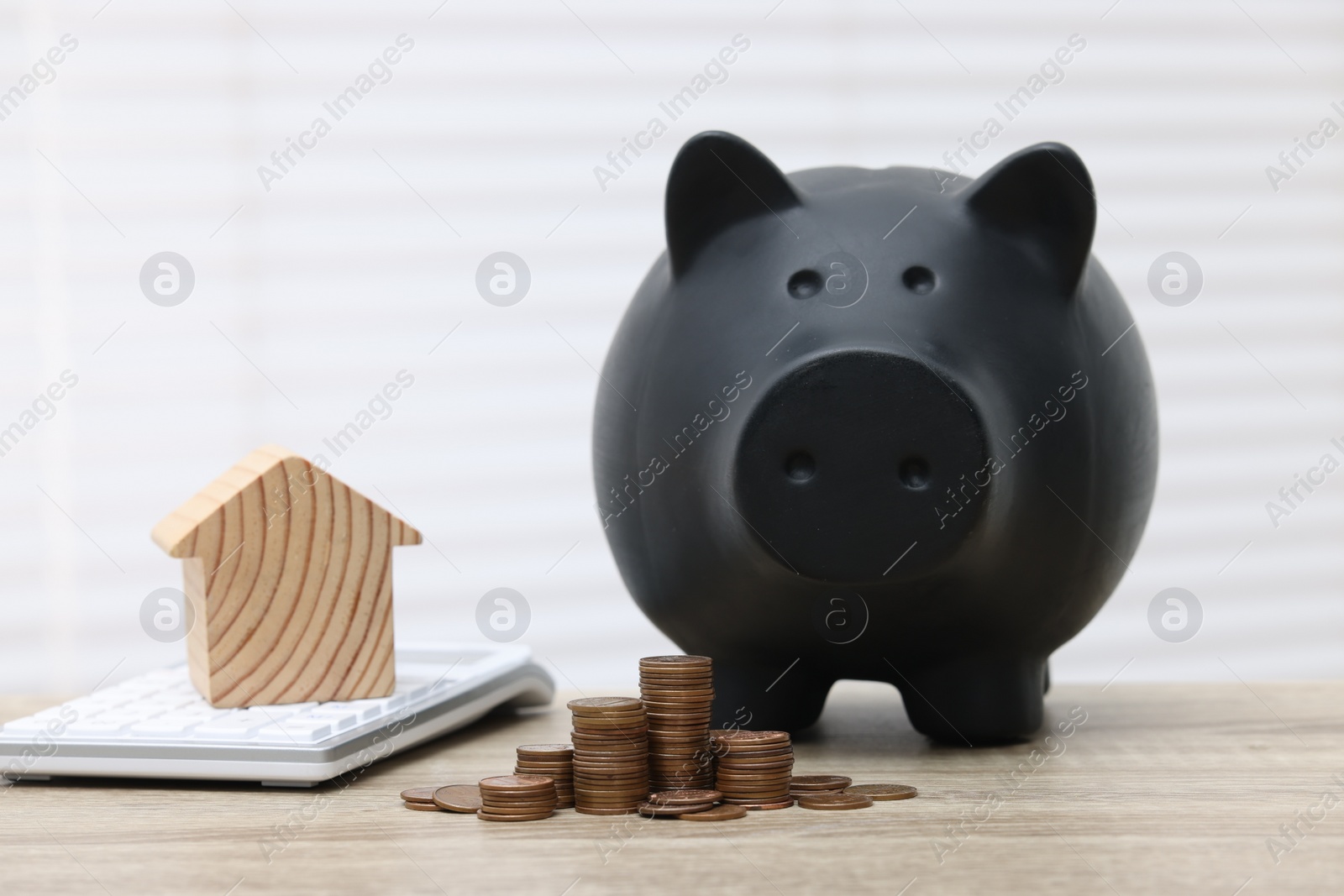 Photo of House model, calculator, piggy bank and stacked coins on wooden table