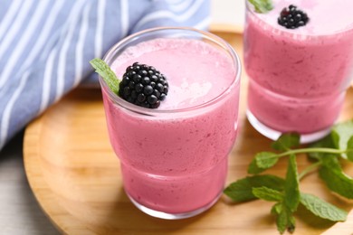 Photo of Delicious blackberry smoothie in glasses on wooden tray, closeup
