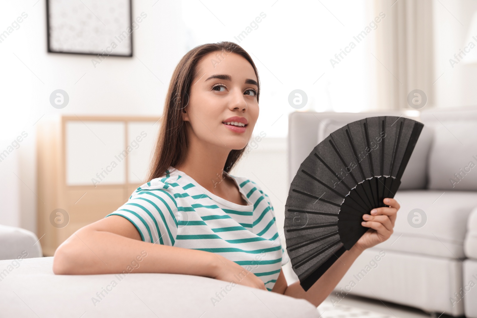 Photo of Woman enjoying air flow from hand fan at home. Summer heat