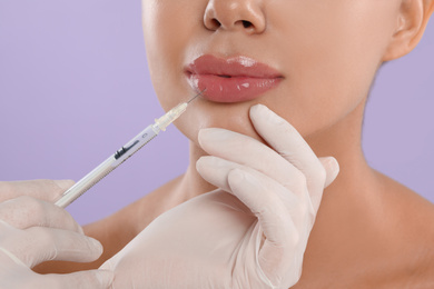 Photo of Young woman getting lips injection on lilac background, closeup