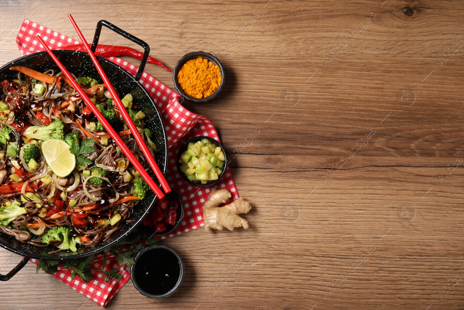 Photo of Stir-fry. Tasty noodles with meat in wok, chopsticks and ingredients on wooden table, flat lay. Space for text