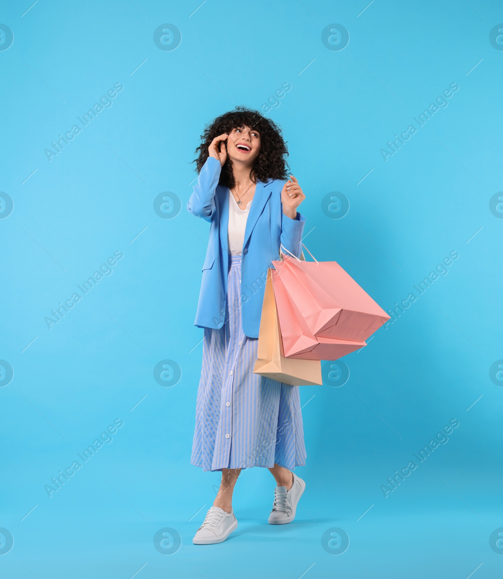 Photo of Happy young woman with shopping bags on light blue background. Space for text