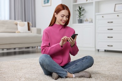 Photo of Happy woman sending message via smartphone on floor at home