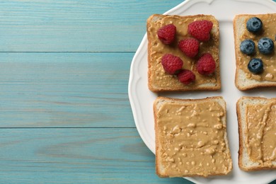 Photo of Delicious toasts with peanut butter, raspberries and blueberries on light blue wooden table, top view. Space for text