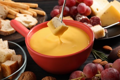 Photo of Dipping piece of bread into tasty cheese fondue at black table, closeup