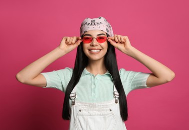 Young woman wearing stylish bandana and sunglasses on pink background