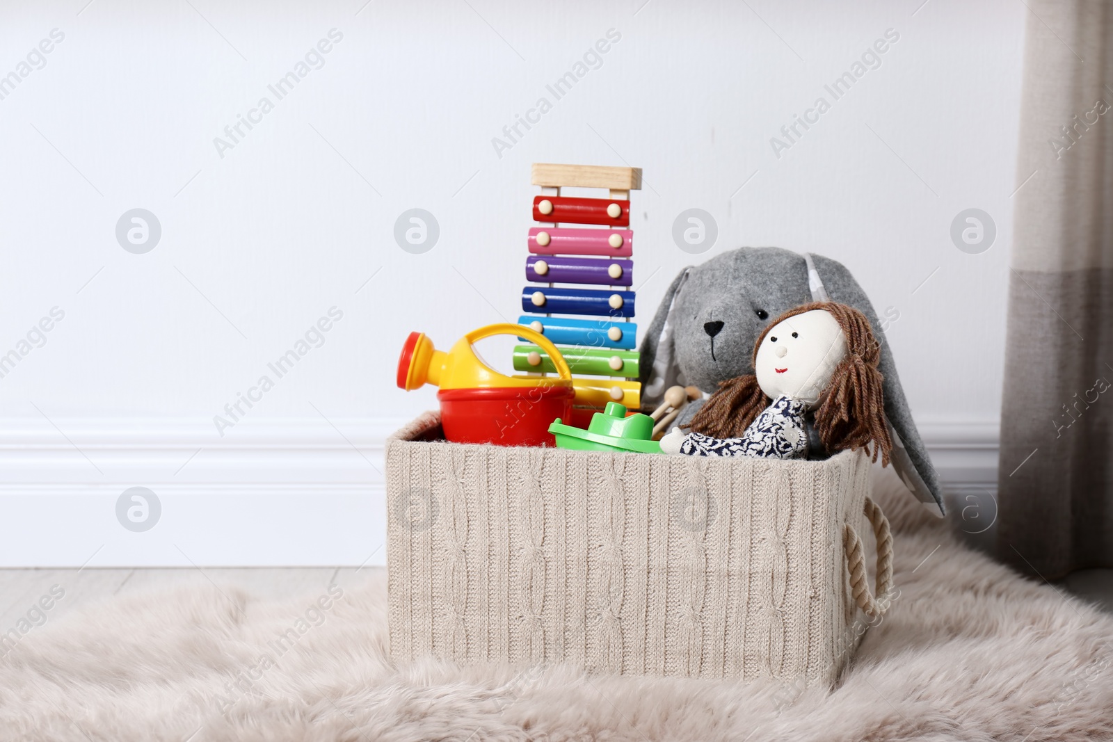 Photo of Box with different child toys on floor against white wall. Space for text