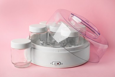 Modern yogurt maker with empty jars on pink background