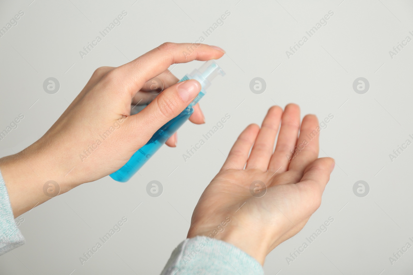 Photo of Woman applying antiseptic gel on light grey background, closeup