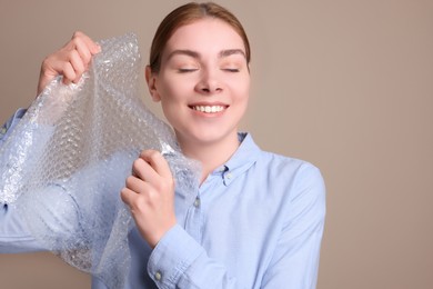 Woman popping bubble wrap on beige background. Stress relief