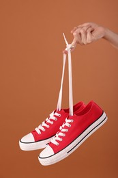 Photo of Woman holding pair of red classic old school sneakers on brown background, closeup