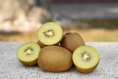 Photo of Whole and cut fresh kiwis on white table with pattern outdoors