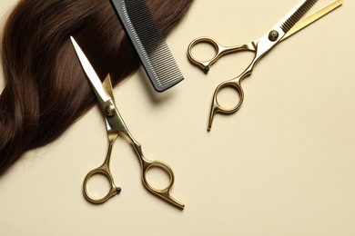 Photo of Professional scissors and comb with brown hair strand on beige background, flat lay. Space for text