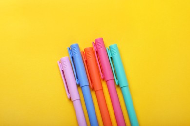 Many colorful markers on yellow background, flat lay