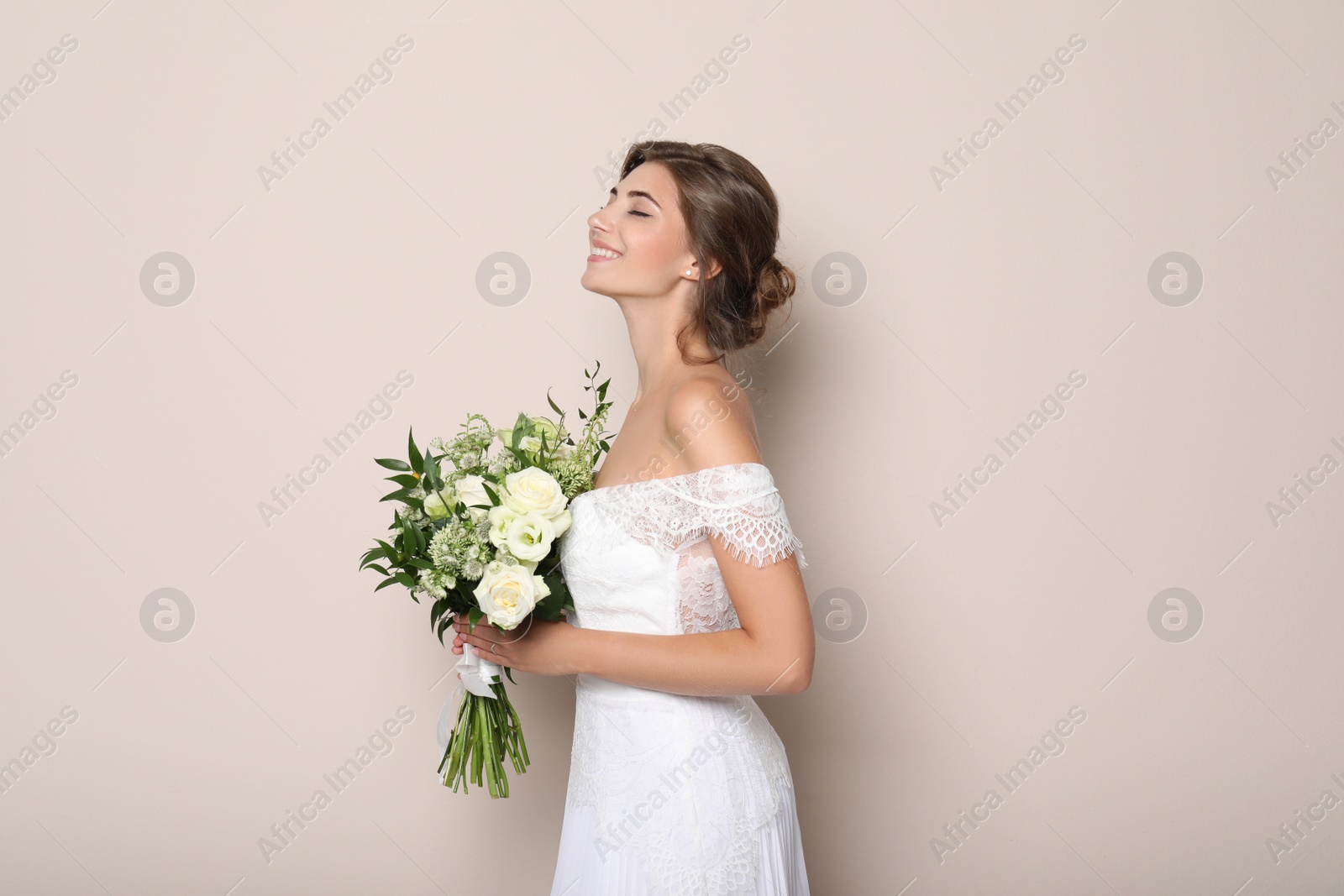 Photo of Young bride wearing wedding dress with beautiful bouquet on beige background