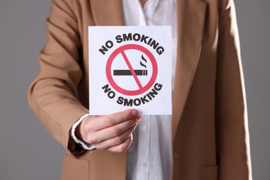 Photo of Woman holding card with no smoking sign on gray background, closeup