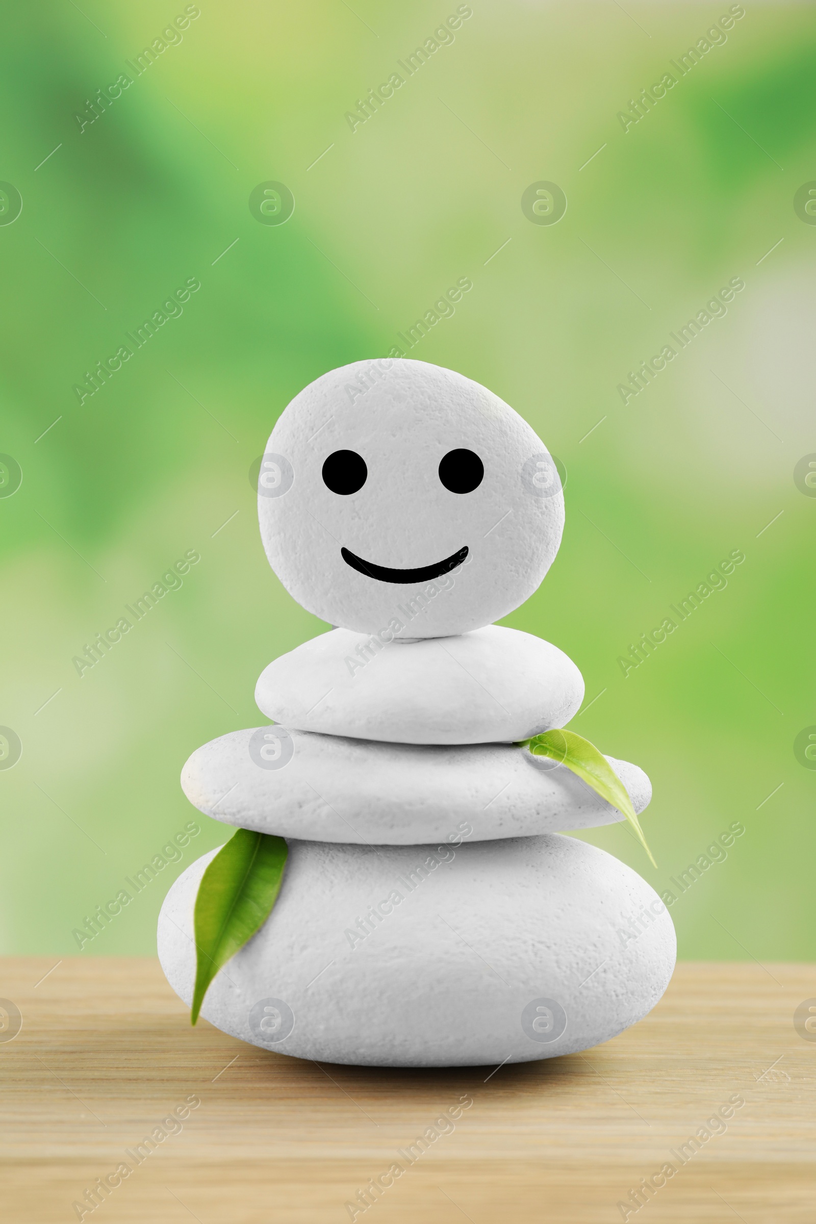 Photo of Stack of stones with drawn happy face and leaves on wooden table against blurred background. Zen concept