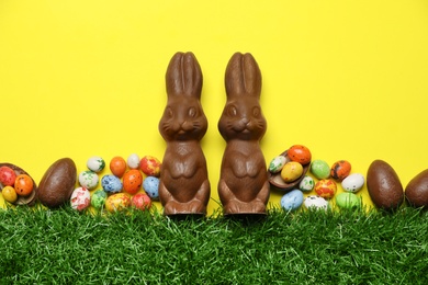 Chocolate Easter bunnies, egg and candies with green grass on yellow background