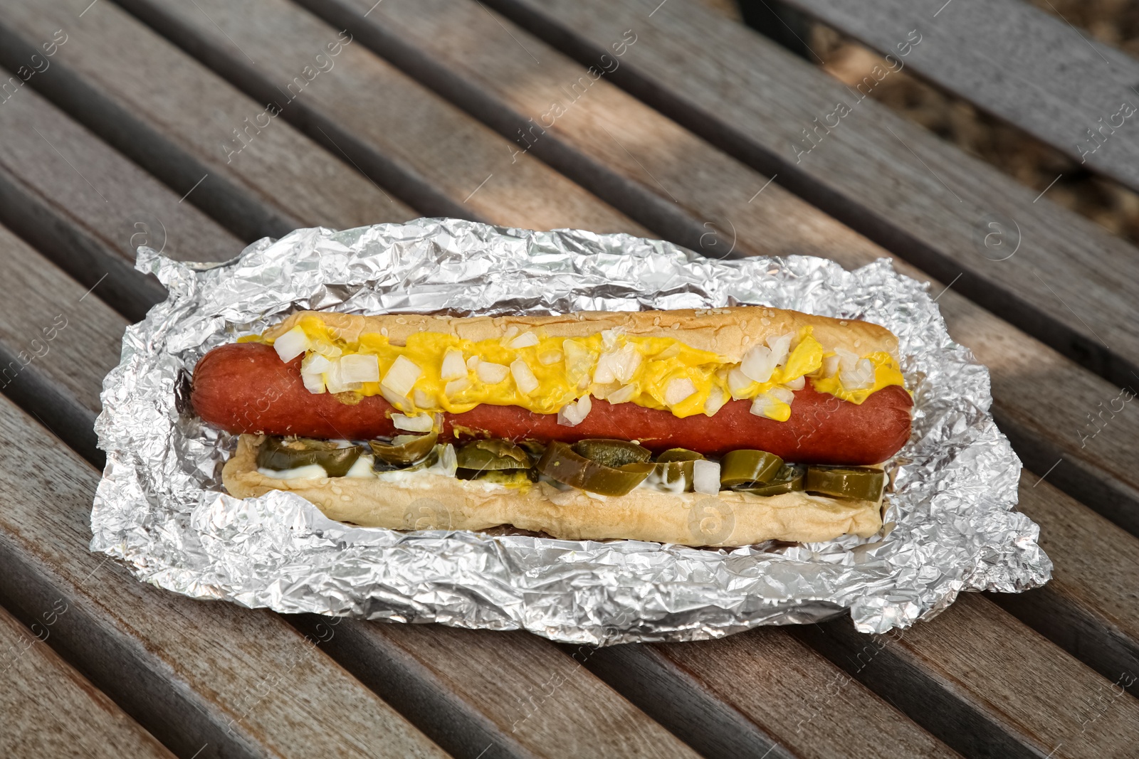 Photo of Fresh tasty hot dog with sauce on wooden surface outdoors