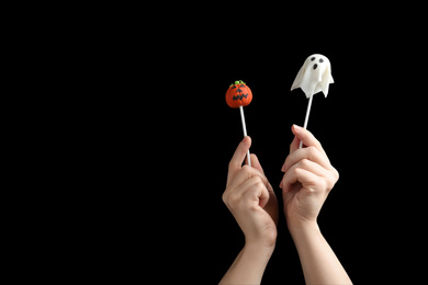 Photo of Woman with delicious cake pops and space for text on black background, closeup. Halloween celebration