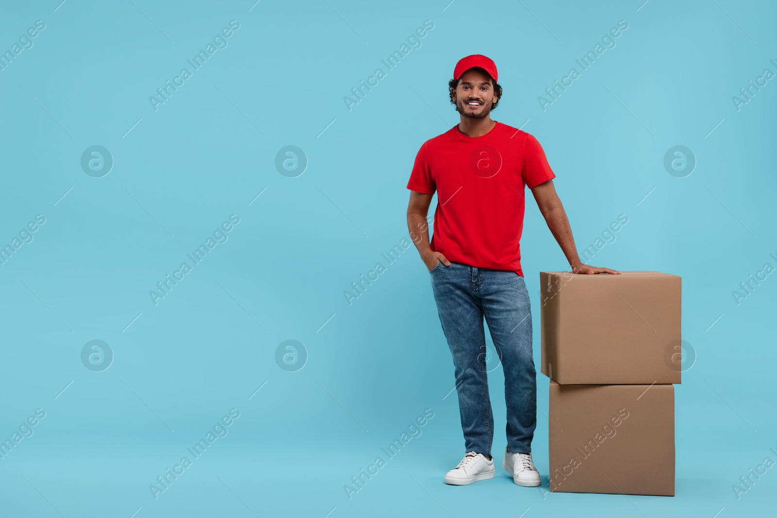 Photo of Happy courier with parcels on light blue background, space for text
