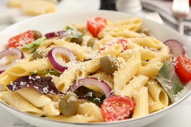 Bowl of delicious pasta with tomatoes, olives and onion on white marble table, closeup